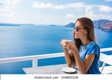 Happy Asian woman drinking coffee enjoying summer vacation at luxury hotel cafe with amazing landscape view of Oia, Santorini. Europe travel destination. Tourist lifestyle.