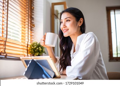 Happy Asian woman drinking coffee and using digital tablet to working remotely from home or online shopping. student study e-learning. social distance preventing Coronavirus or Covid-19. copy space - Powered by Shutterstock