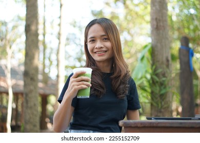 Happy Asian woman drinking green tea in a cafe background with green trees - Shutterstock ID 2255152709