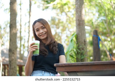 Happy Asian woman drinking green tea in a cafe background with green trees - Shutterstock ID 2255152715