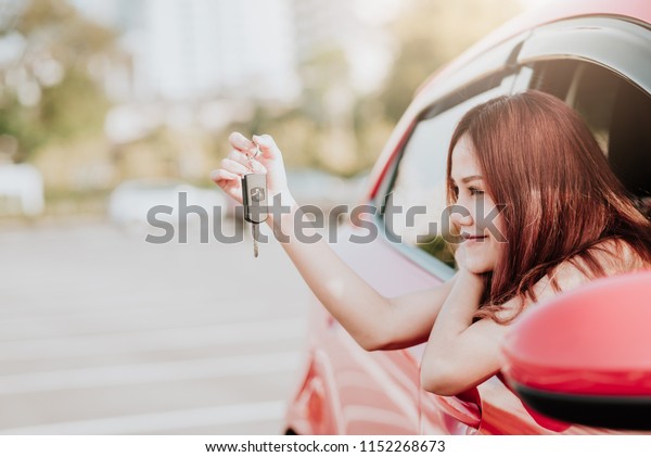 Happy\
Asian woman driver holding car key in her new\
car