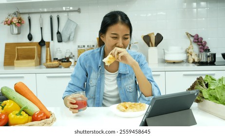 Happy asian woman eating healthy food drinks watch online movie. Women enjoy video call web conference live streaming home kitchen use digital tablet. Female use smart phone online call social media - Powered by Shutterstock