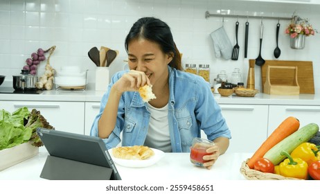 Happy asian woman eating healthy food drinks watch online movie. Women enjoy video call web conference live streaming home kitchen use digital tablet. Female use smart phone online call social media - Powered by Shutterstock