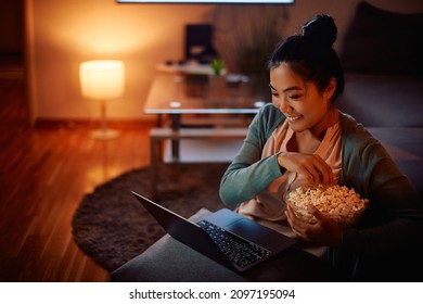 Happy Asian woman eating popcorn while watching her favorite series online on laptop in the evening at home. - Shutterstock ID 2097195094