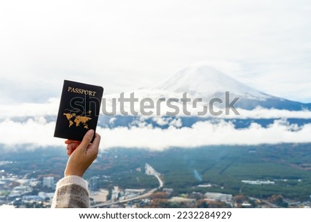 Happy Asian woman enjoy and fun outdoor lifestyle travel Japan on holiday vacation. Woman hand showing passport with Mt Fuji covered in snow and beautiful nature of lake Kawaguchi in autumn background