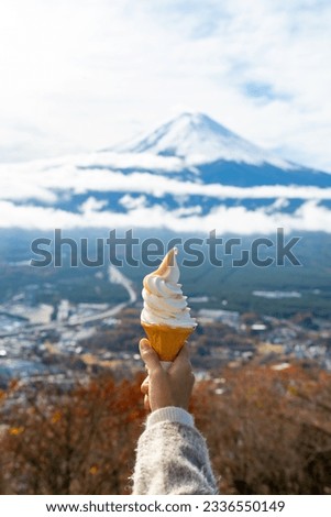 Happy Asian woman enjoy and fun outdoor lifestyle travel Japan on holiday vacation. Attractive girl hand holding ice cream cone while  travel at Mt.Fuji covered in snow and lake Kawaguchi in autumn.