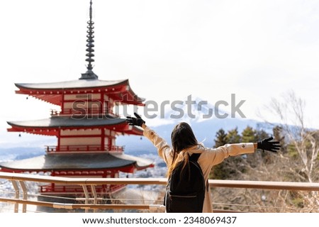 Happy Asian woman enjoy outdoor lifestyle travel at red Chureito Pagoda with Mt Fuji covered background in winter holiday vacation. People travel Japan landmark famous place and season change concept.