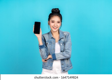 Happy asian woman feeling happiness and standing hold smartphone on blue background. Cute asia girl smiling wearing casual jeans shirt and connect internet shopping online and present