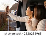 Happy Asian woman friend enjoy outdoor lifestyle using mobile phone taking selfie together on car trunk during road trip travel Japan landmark Kawaguchi lake and Mt Fuji on autumn holiday vacation.