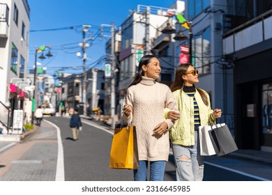Happy Asian woman friends walking and shopping together at Shibuya district, Tokyo, Japan in autumn. Attractive girl enjoy and fun outdoor lifestyle walking and travel city street on holiday vacation.