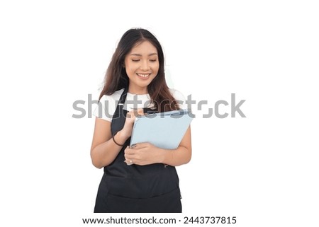 Happy Asian woman as groceries or modren market staff checking products and goods on the display shelf while holding tablet and wearing black apron isolated white background