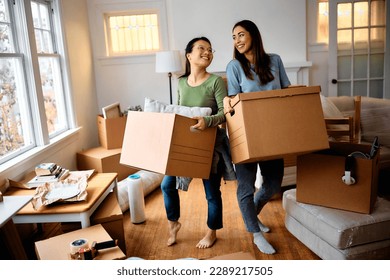 Happy Asian woman and her female friend carrying cardboard boxes into their new apartment.  - Powered by Shutterstock