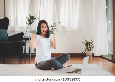 Happy Asian Woman Holding Dumbbells In Both Hand Feeling Ready To Exercises Workout At Home With Laptop 