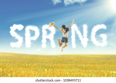 Happy Asian woman holding hat jumping on meadow. Summer or spring concept