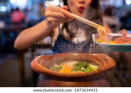 Happy Asian woman holding raw meat with chopsticks in shabu hotpot restaurant. Young girl making wow mouth eating dinner with copy space
