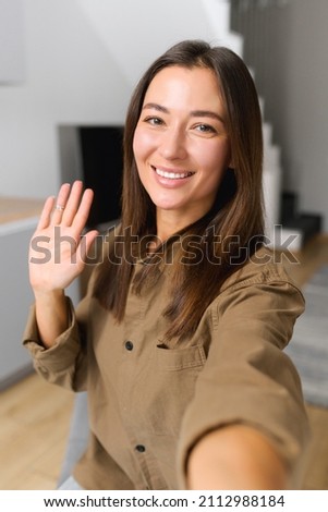 Happy asian woman holding smartphone and waving with hand to the camera while having video call with somebody. People and technologies concept