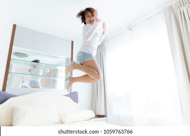 Happy Asian woman jump on the bed in a white bedroom.