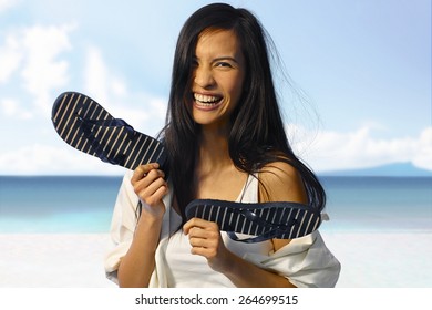 Happy Asian Woman Laughing On The Beach At Summertime, Holding Flip Flop In Hand.