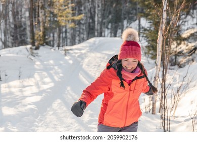 Happy Asian woman laughing walking in snow forest during winter. Beautiful portrait of young adult smiling wearing cold weather hat and gloves, orange jacket.