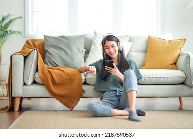 Happy asian woman listening to music from mobile phone while sitting on the rug beside to the sofa at homes, Smiling girl relaxing with headphones in morning, Time to relax. - Shutterstock ID 2187590537