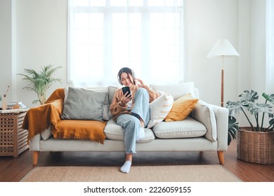Happy asian woman listening to music from mobile phone while sitting on the the sofa at homes, Smiling girl relaxing with headphones in morning, Time to relax. copy space.