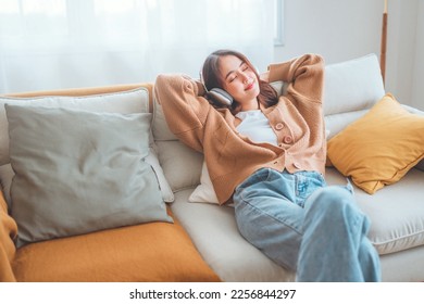 Happy asian woman listening to music from mobile phone while sitting on the the sofa at homes, Smiling girl relaxing with headphones in morning, Time to relax. copy space. - Powered by Shutterstock