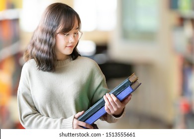 Happy Asian woman looking for a book in an university library. Woman reading book in a library. Library and Education concept.