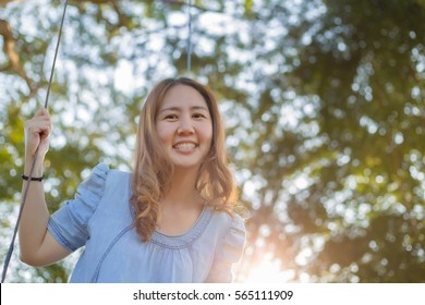 Happy Asian woman playing swing outdoor in the park