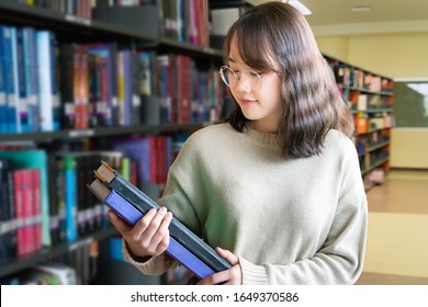 Happy Asian Woman reading book in a library. Woman looking for a book in an university library. Library and Education concept.