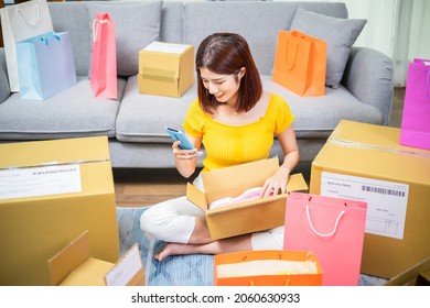 Happy Asian Woman Receive Packing Parcel After Online Shopping At Home And She Check Order List On Mobile Phone In Opening Delivery Boxes