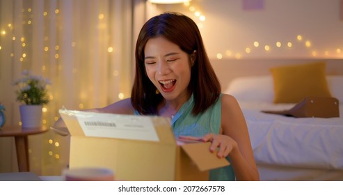 Happy asian woman receive packing parcel after online shopping in the evening at home and opening a delivery box