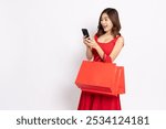 Happy Asian woman in red dress using mobile phone and holding shopping bag isolated on white background, Shopping online on application in smartphone concept