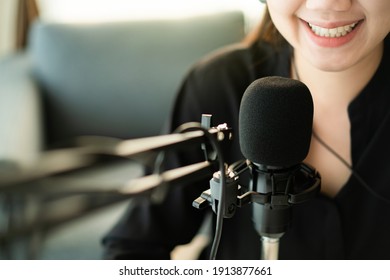 Happy Asian Woman Setting Up A Living Room In Her House For Podcast Studio, Woman Arranging A Podcast And Online Radio Station At Home. Professional Young Podcaster Speaking Through A Microphone.