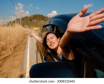 Happy Asian Woman With Short Hair Closing Her Eyes And Raising Hands Feeling The Freedom While Traveling By Car. Attractive Female Travelers Enjoy And Smiling At The View Outside The Car, On The Road.