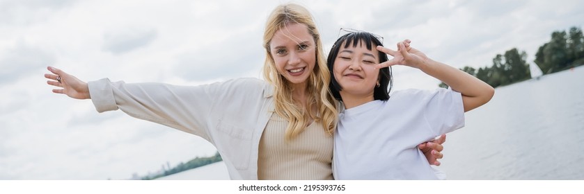 Happy Asian Woman Showing Peace Sign Near Blonde Friend, Banner