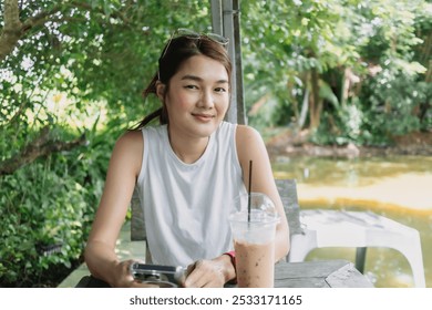 Happy Asian woman sitting in the pond garden with iced coffee. - Powered by Shutterstock