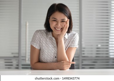Happy asian woman sitting at table, looking at camera, having video call with friend or client, listening speaker, laughing at joke. Positive young female hr manager holding distant job interview.