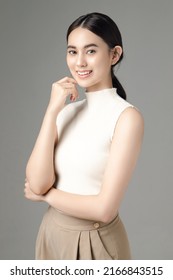 Happy Asian Woman Smile Touch Her Chin And Looks At The Camera Isolated Over Grey Background. Portrait Of Pretty Girl In Studio.