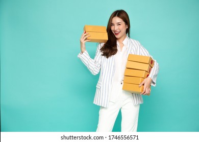 Happy Asian Woman Smiling And Holding Package Parcel Box Isolated On Light Green Background, Delivery Courier And Shipping Service Concept