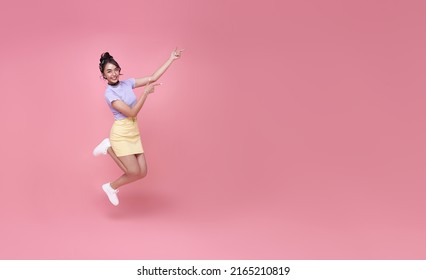 Happy Asian woman smiling and jumping while hands pointing isolated over pink background. copy space