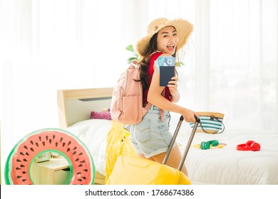 Happy Asian woman smiling while showing passport and plane ticket with many items to preparing to traveling beach trip on weekend. Young pretty woman with suitcase going to travel on holiday.