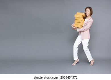 Happy Asian woman standing and holding package parcel box isolated on grey background, Delivery courier and shipping service concept