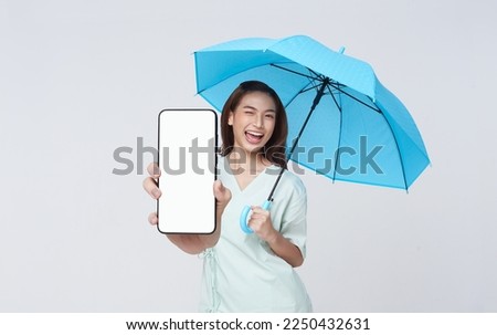 Happy Asian woman standing holding blue umbrella and showing smartphone isolated on white background, application service life insurance and protection concept.