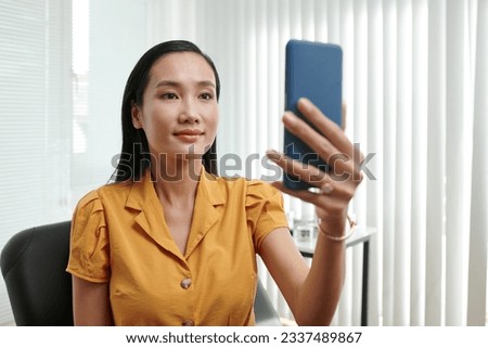 Happy Asian woman taking selfie after getting refreshing beauty procedure in clinic