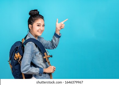 Happy asian woman travel backpacker standing pointing hands to copyspace on blue background. Cute asia girl smiling wearing casual jeans shirt and finger pointing to aside for present promotions. - Shutterstock ID 1646379967