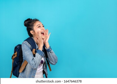 Happy Asian Woman Travel Backpacker Shouting Open Mouth To Copyspace On Blue Background. Cute Asia Girl Smiling Wearing Casual Jeans Shirt And Looking To Aside For Present Promotions.