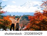 Happy Asian woman travel Japan Fuji on holiday vacation. Attractive girl friends using mobile phone taking selfie during travel Mt.Fuji and looking beautiful red maple tree leaf falling down in autumn