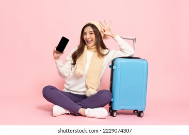 Happy Asian woman traveler sitting on floor with luggage and holding mobile phone isolated on pink background, Tourist girl having cheerful holiday trip concept, Full body composition - Shutterstock ID 2229074307