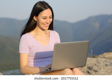 Happy Asian Woman Using Laptop Sitting On A Cliff In The Mountain