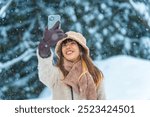 Happy Asian woman using mobile phone taking selfie or vlogging during travel nature forest mountain in snow day. Attractive girl enjoy outdoor lifestyle travel countryside on winter holiday vacation.